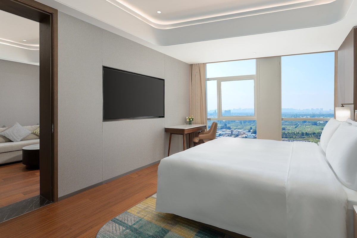 Een hotelkamer met een groot bed, een bureau, een televisie en uitzicht op de stad.