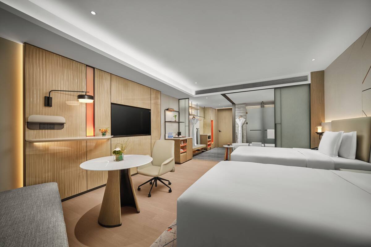 A modern hotel room with a large bed, a desk, a chair, a TV, and a small table with a plant.