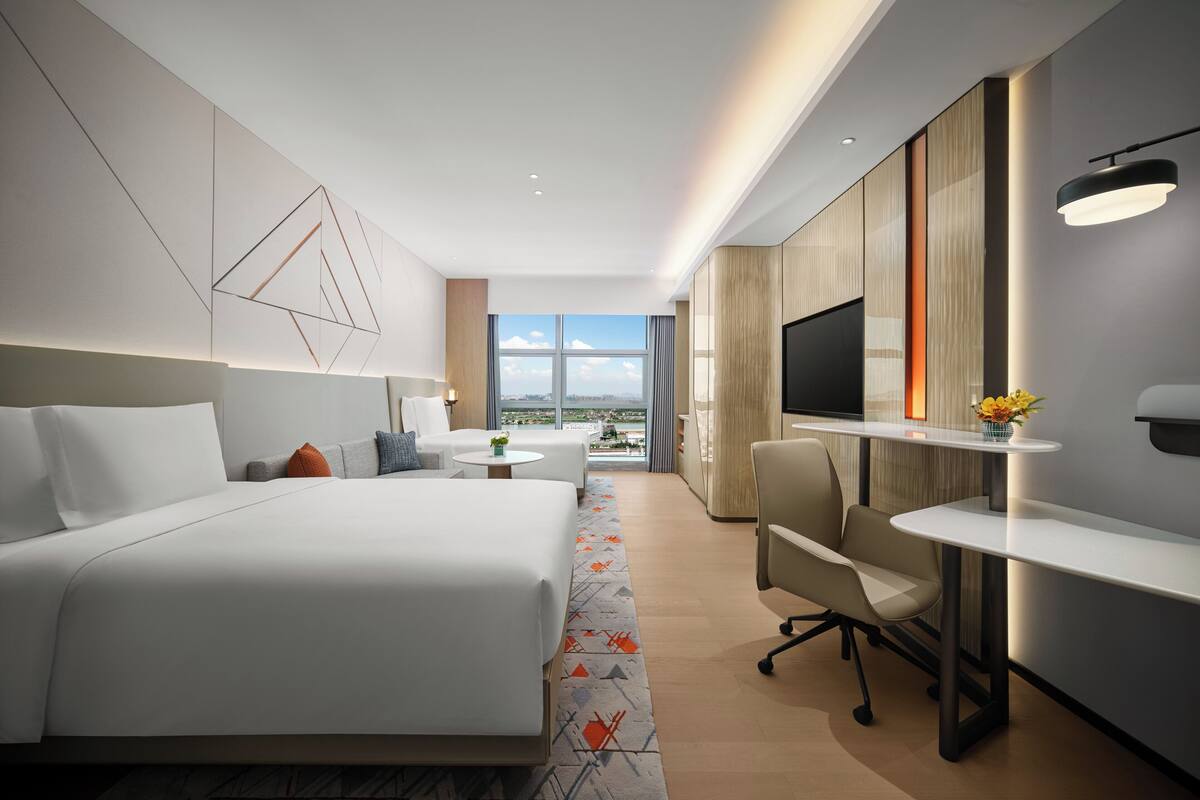 A modern hotel room with a large bed, a desk, a TV, and a view of the city.