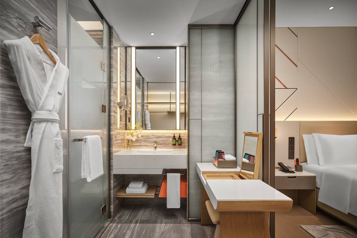 A modern bathroom with a glass shower enclosure, a vanity with a mirror, and a bedside table with a lamp.