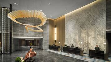 A modern hotel lobby with a central reception desk, a unique spiral light fixture, and a marble wall.