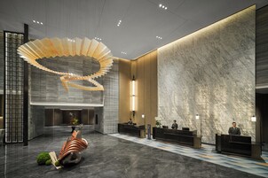 A modern hotel lobby with a central reception desk, a unique spiral light fixture, and a marble wall.
