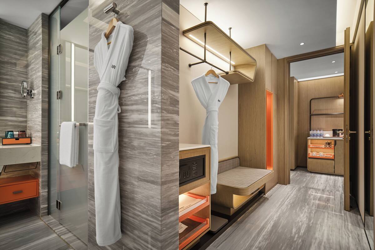 A modern bathroom with a glass shower, a robe hanging on the wall, a built-in bench, and a vanity with a mirror.
