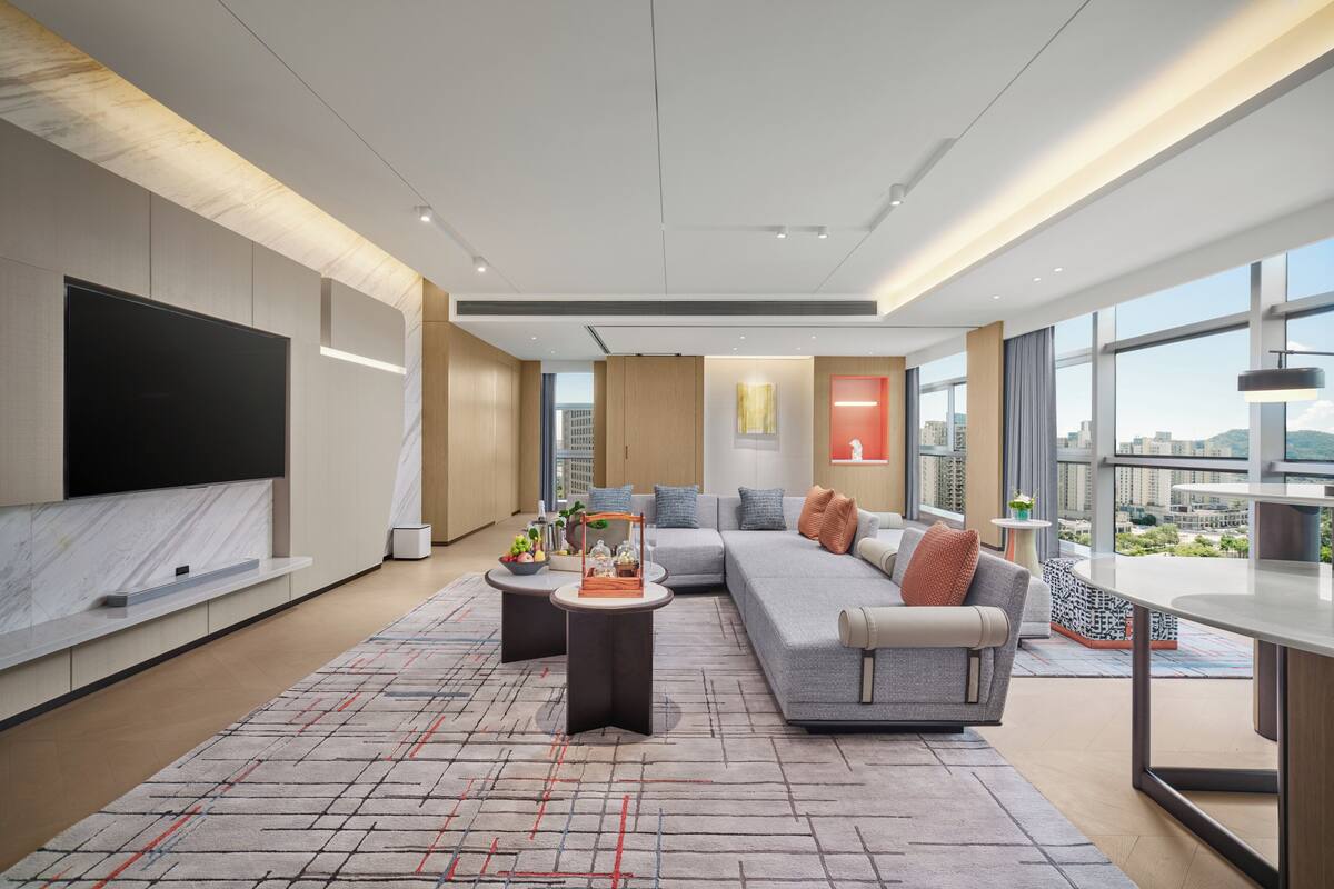 A modern living room with a large flat-screen TV, a sectional sofa, and a dining area with a view of the city.