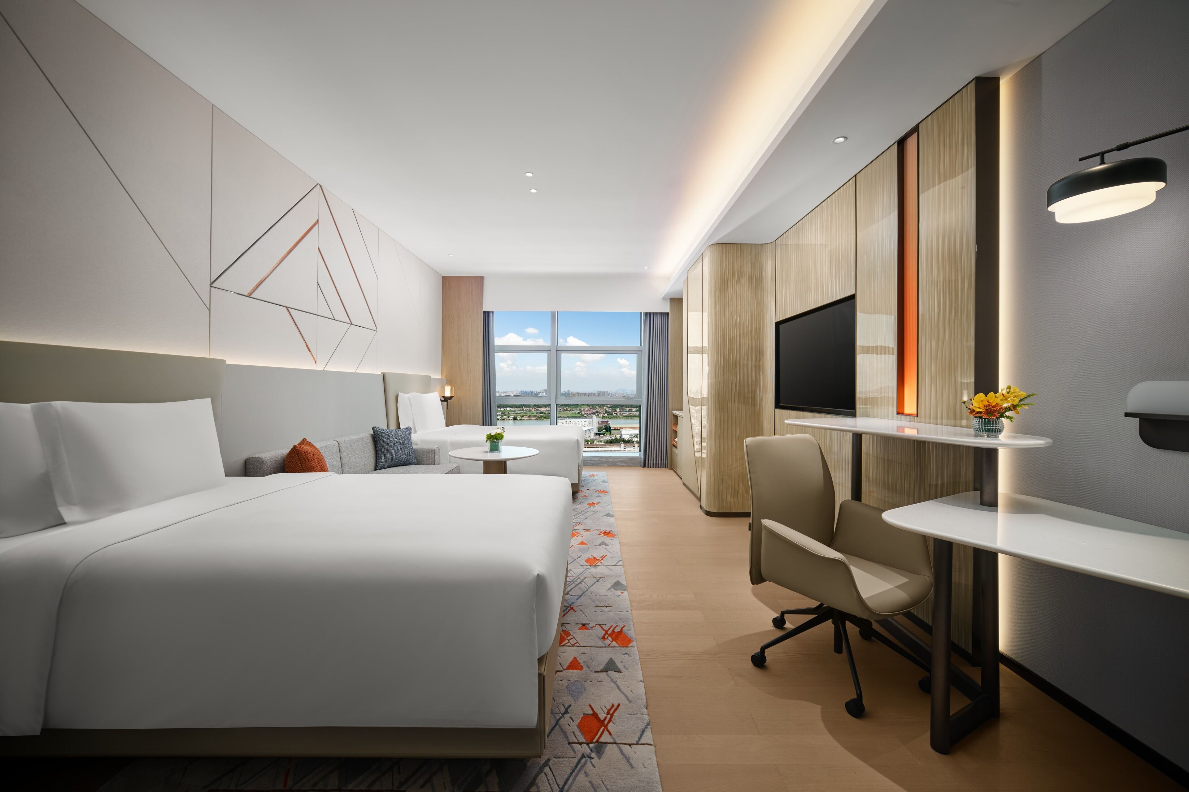 Ein modernes Hotelzimmer mit einem großen Bett, einem Schreibtisch, einem Fernseher und Blick auf die Stadt.