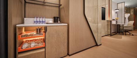 A modern hotel room with a wooden cabinet, a small table with a plant, and a desk with a chair.