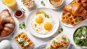 Un desayuno con huevos, croissants, gofres y una ensalada verde.