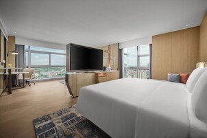 Una habitación de hotel moderna con una cama grande, un televisor de pantalla plana, un escritorio con silla y vistas a la ciudad.