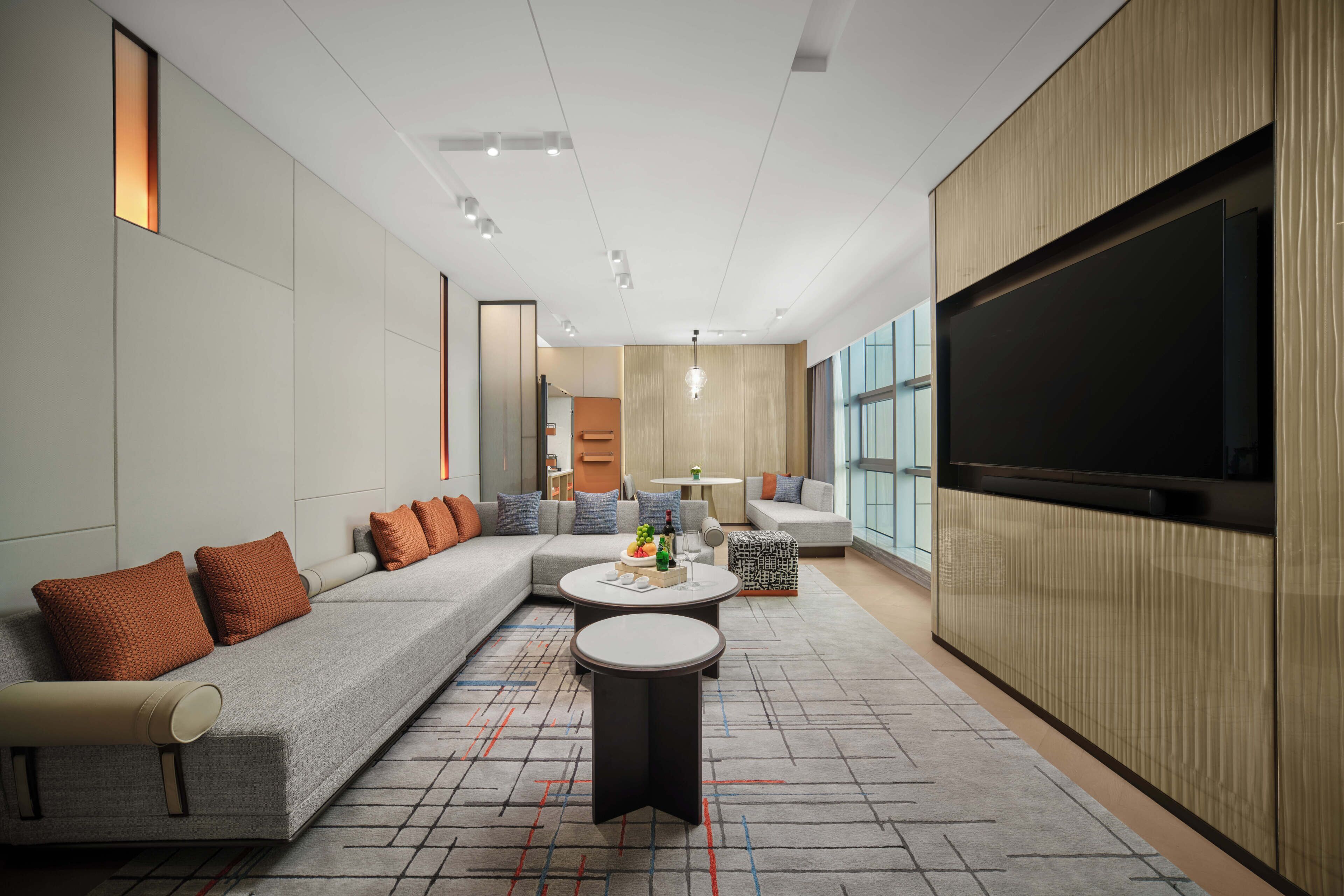 A modern living room with a sectional sofa, a round coffee table, and a large flat-screen TV mounted on the wall.