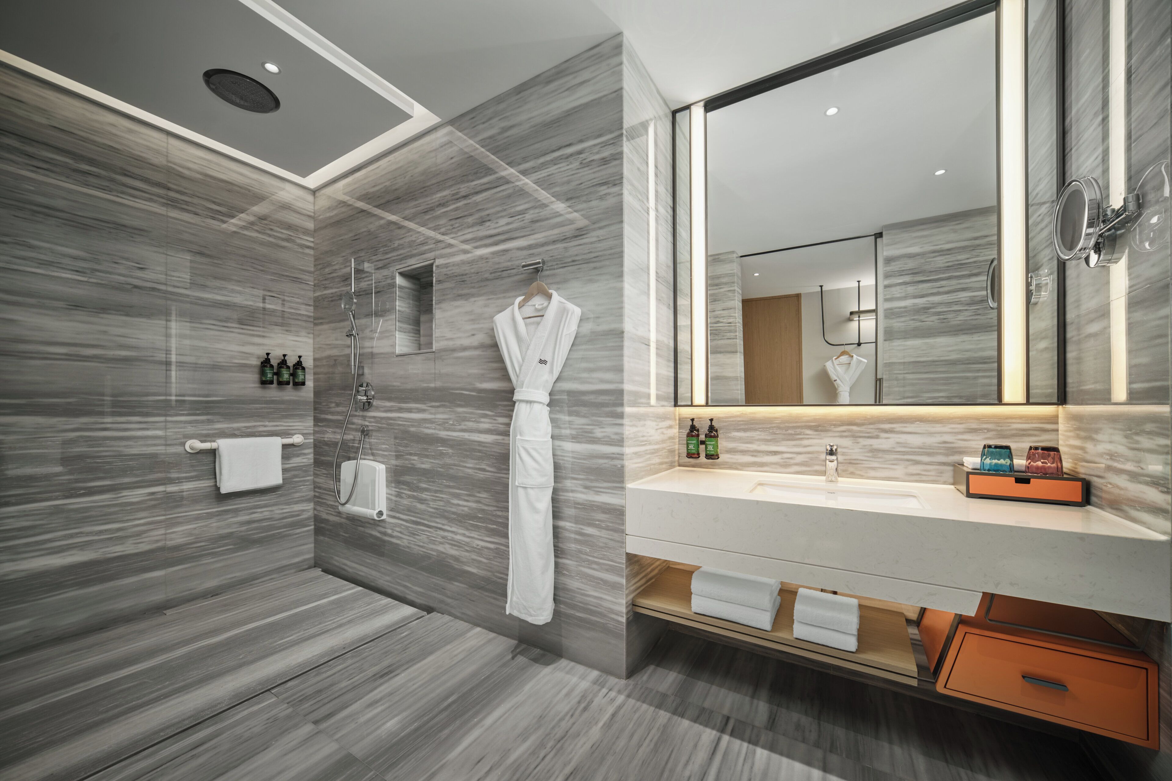 Un baño moderno con pared de mármol, un espejo grande, ducha y tocador con lavabo y perchero para toallas.