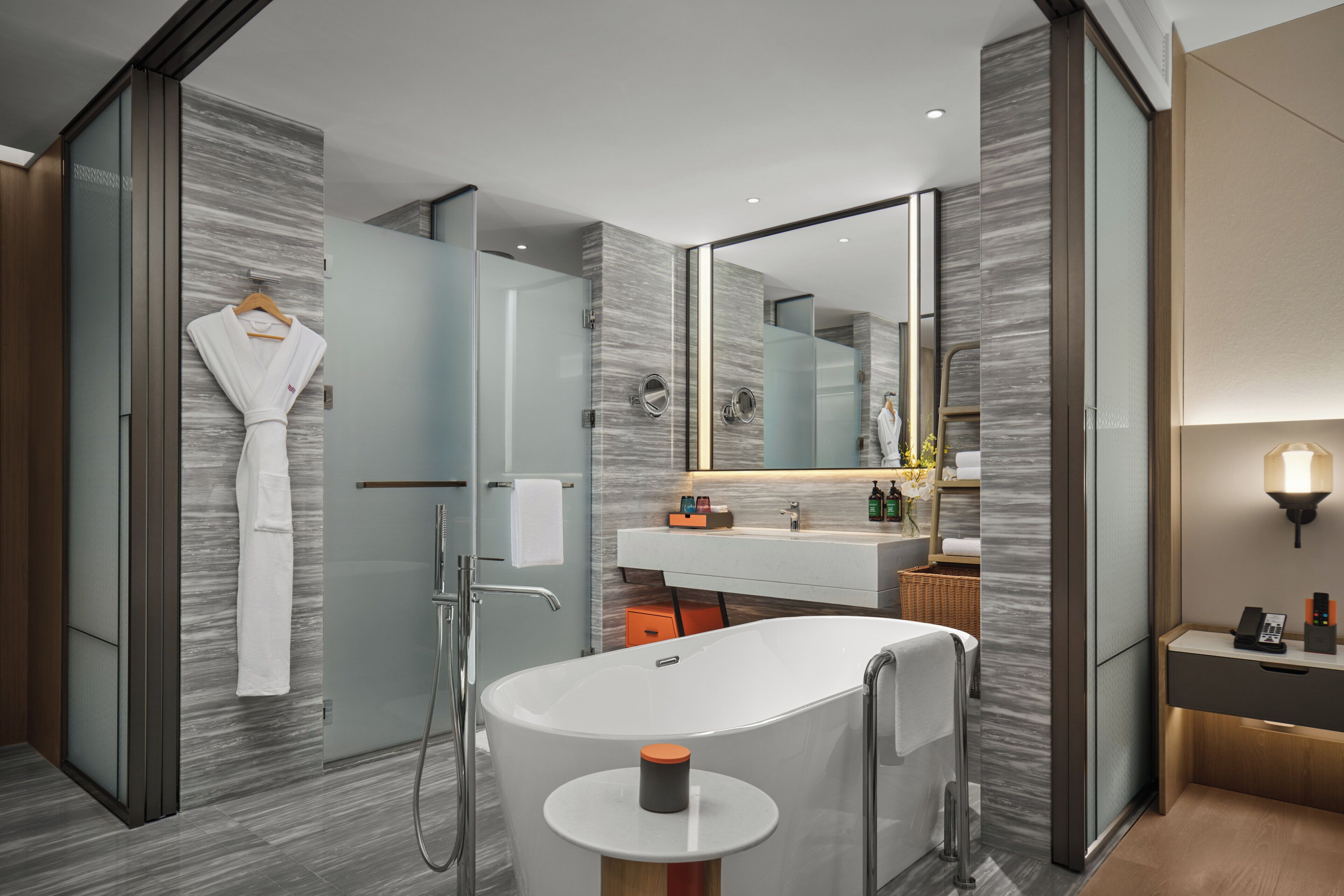 A modern bathroom with a freestanding bathtub, a glass shower enclosure, a vanity with a mirror, and a robe hanging on the wall.