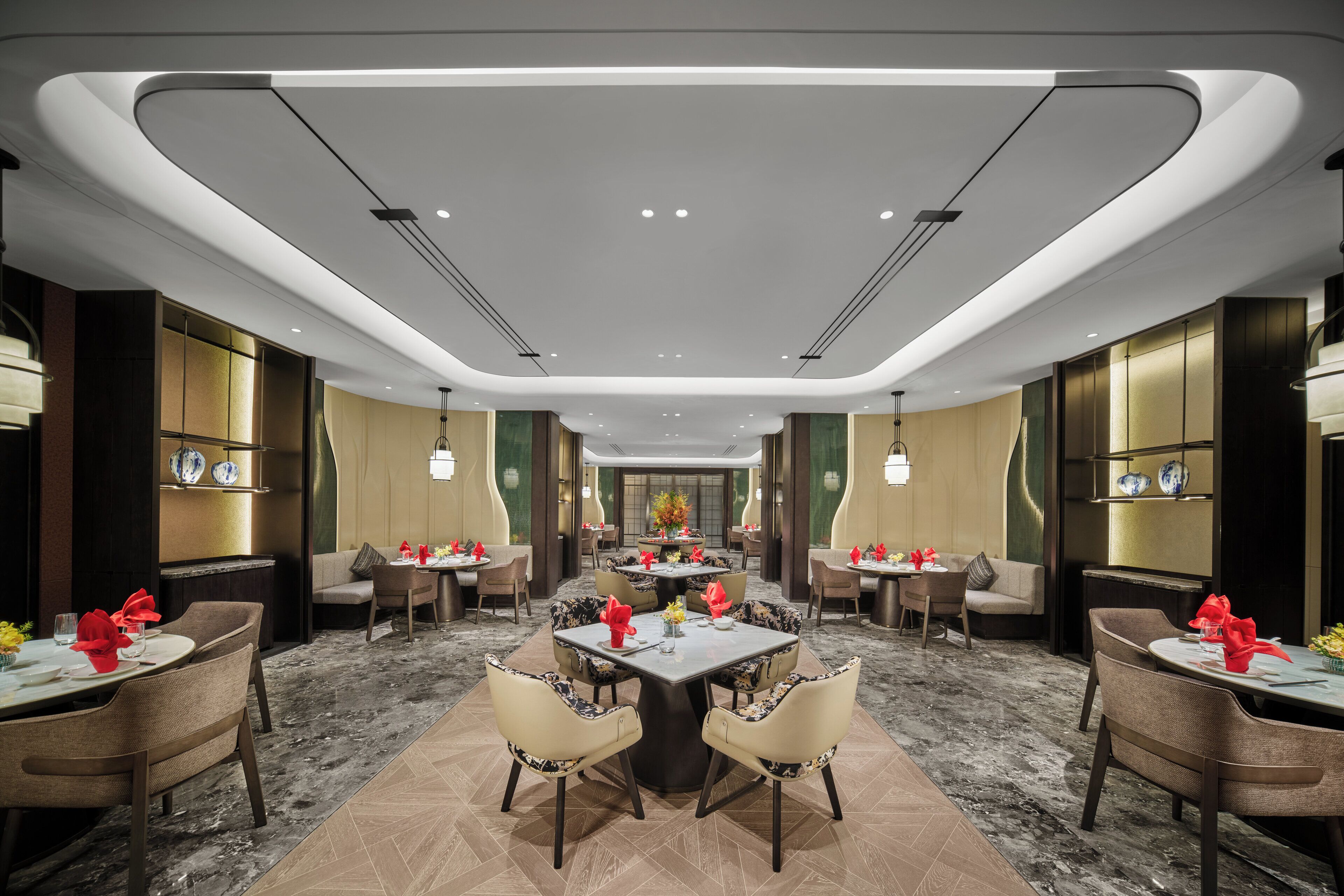 A modern hotel dining area with multiple tables and chairs, a central decorative piece, and a marble floor.