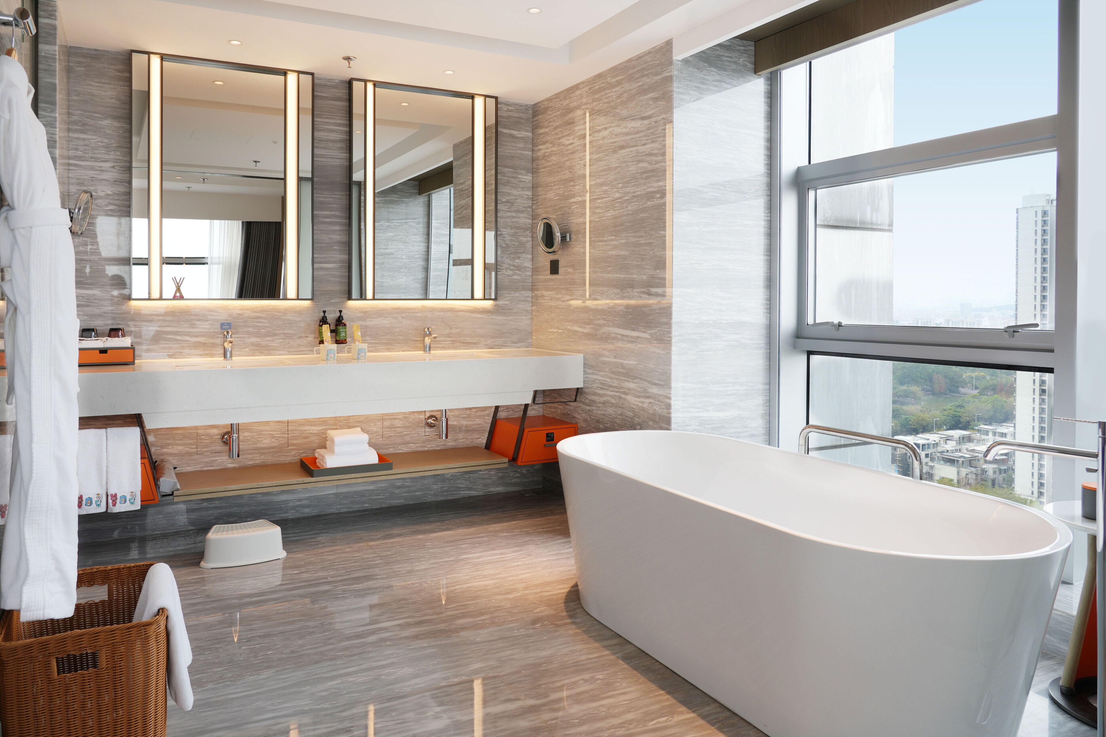 A modern bathroom with a large bathtub, a vanity with a mirror, and a window offering a city view.