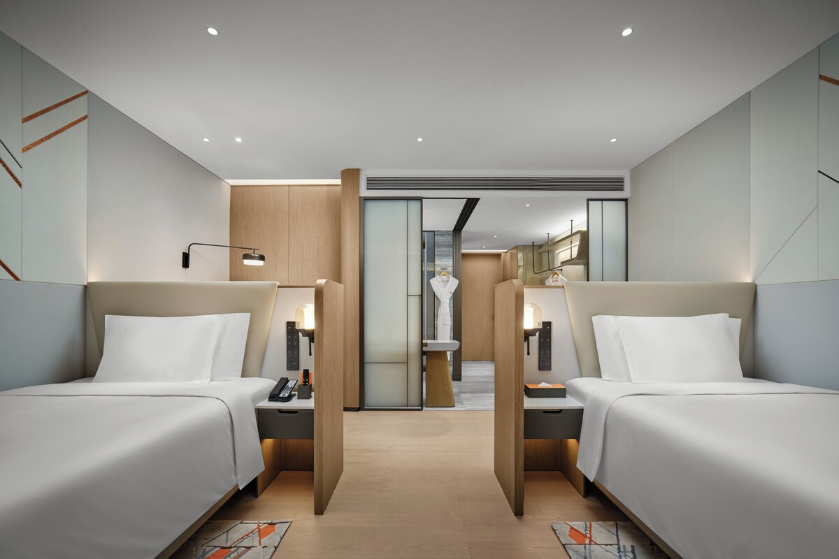 A modern hotel room with two beds, a desk, a phone, and a lamp.