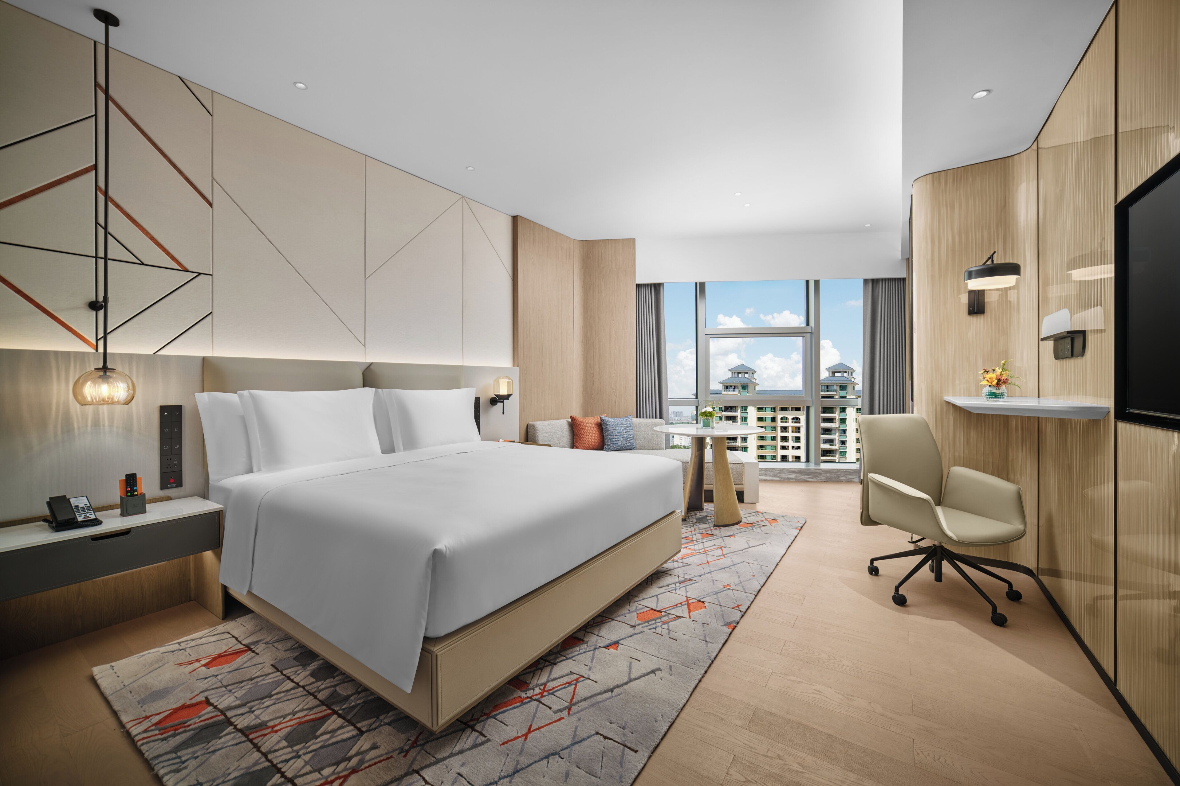 A modern hotel room with a large bed, a desk, a chair, and a TV.