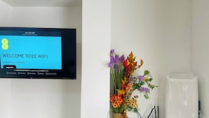 A flat-screen TV displaying the EE WiFi login page, a flower arrangement, and a white printer on a white desk.