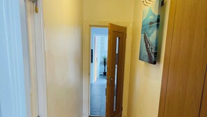 A hallway with wooden flooring, white walls, and a painting of a bridge.