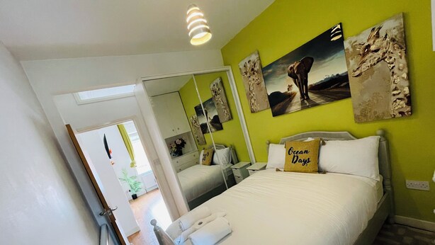 A bedroom with a bed, a nightstand, a mirror, and artwork on the wall.