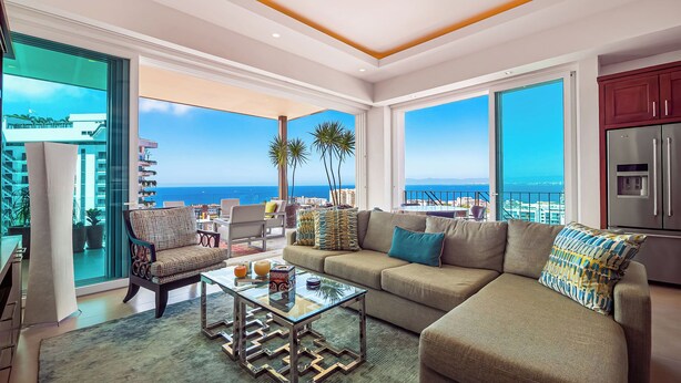 A spacious living room with a large sofa, a glass coffee table, and a view of the ocean.