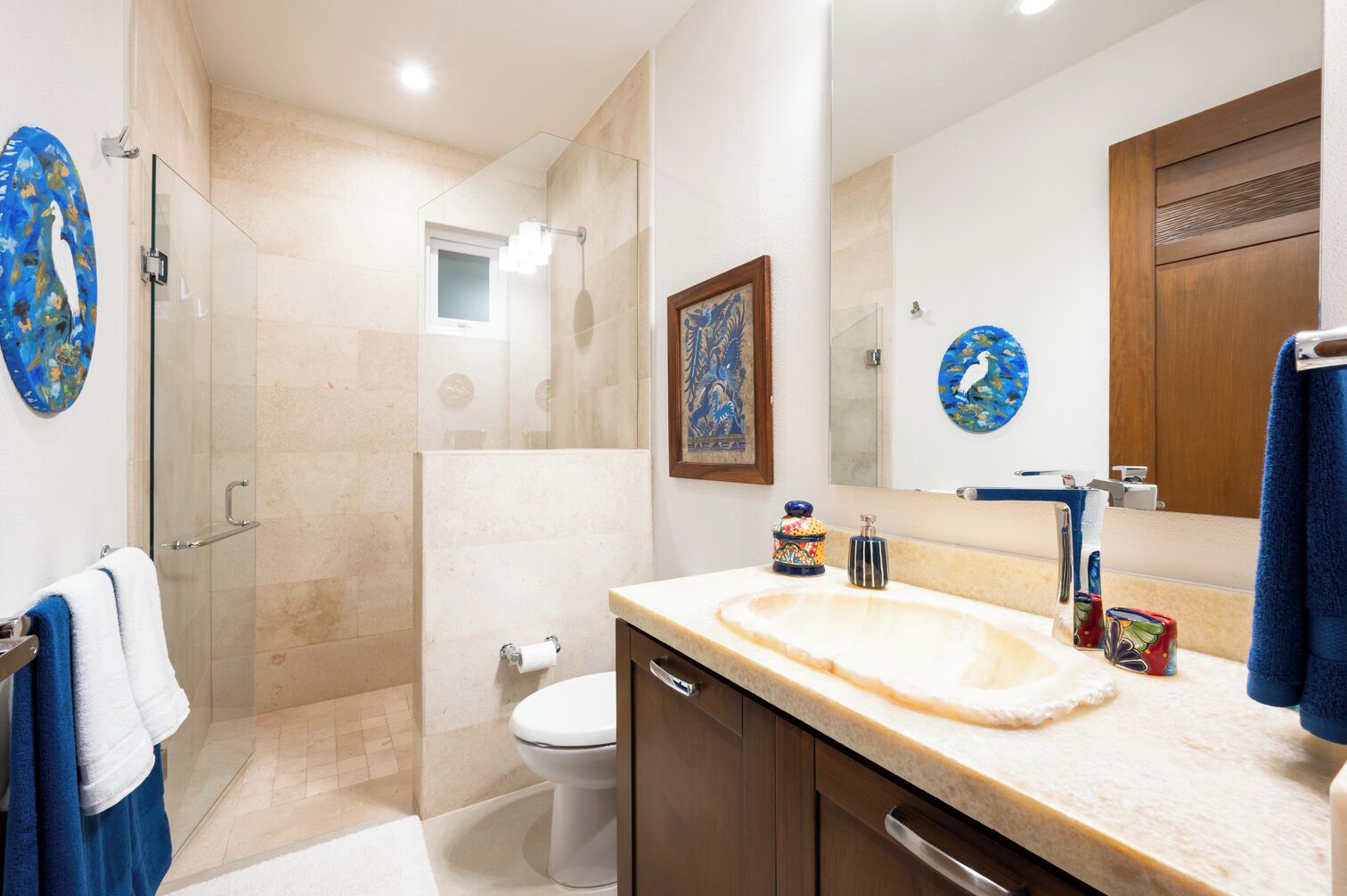 Un baño moderno con cabina de ducha de vidrio, un espejo grande y una encimera color beige.