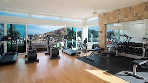 A spacious gym with various exercise equipment, large windows offering a view of a hilly landscape, and a stone accent wall.