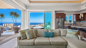 A modern living room with a large sofa, a dining area, and a kitchen.
