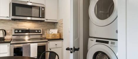 A compact kitchen with a microwave, oven, and stacked washer-dryer unit.