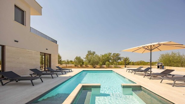 Un área de piscina exterior moderna con sillones de descanso y una parrilla.