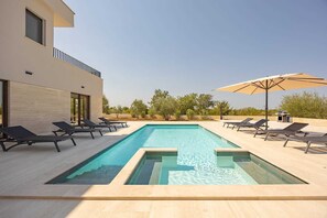 A modern outdoor pool area with lounge chairs and a barbecue grill.
