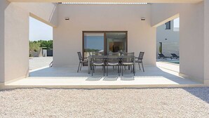 Un área de comedor al aire libre con techo, una mesa y sillas, una puerta corrediza de vidrio y un espacio de descanso junto a la piscina.