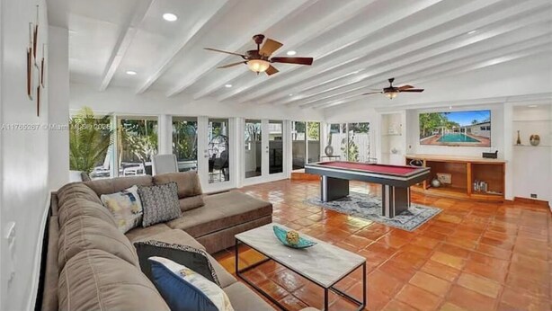 A spacious living room with a pool table, a sofa, and ceiling fans. - LUXTROPICA (Miami)