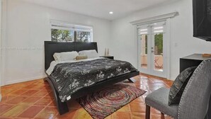 A bedroom with a bed, a chair, a TV, and a sliding glass door leading to an outdoor area. - LUXTROPICA (Miami)