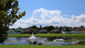 Ein Wohngebiet mit Häusern, einem Teich und einem Springbrunnen, bewölkter Himmel.