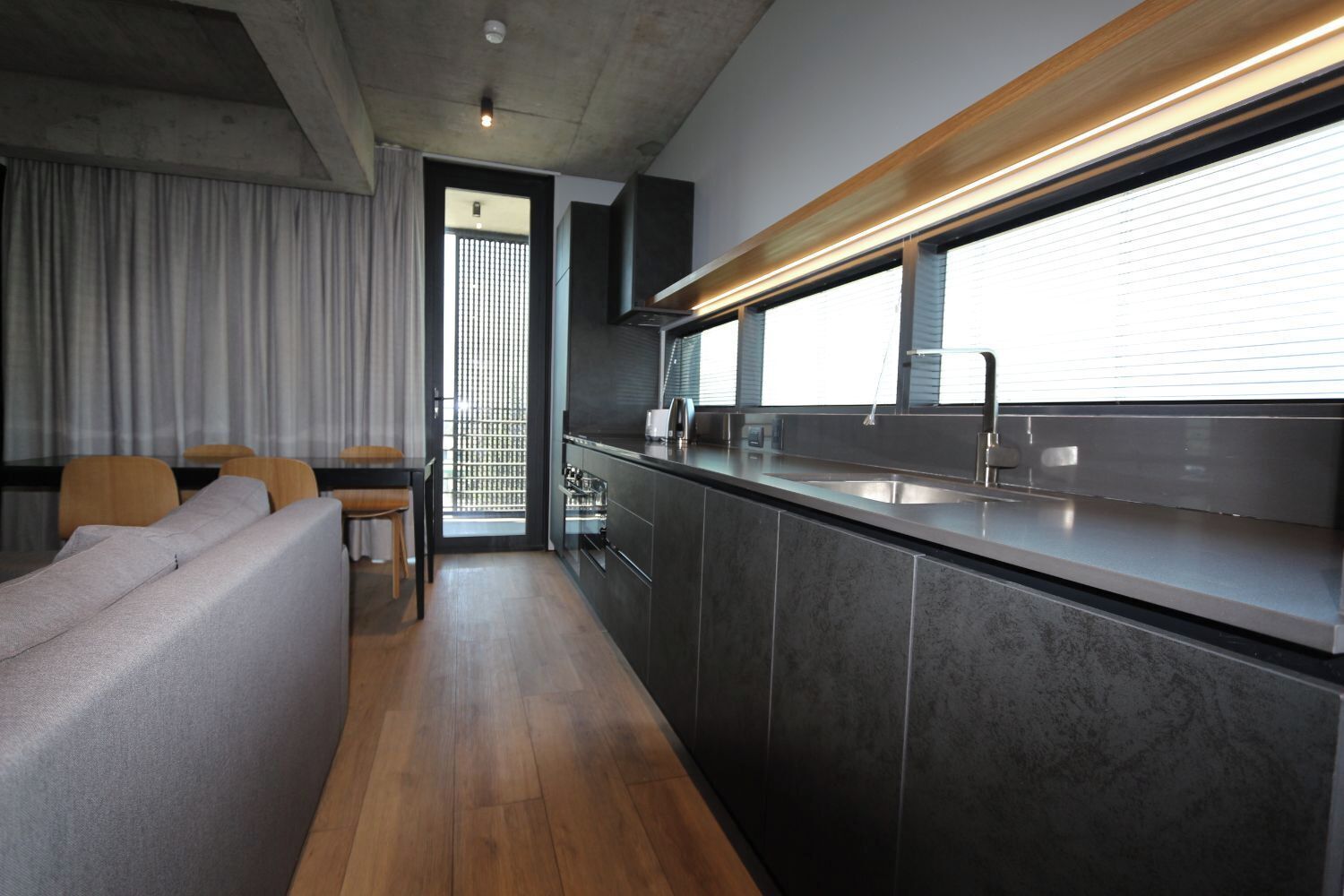 A modern kitchen with dark cabinetry, a wooden countertop, and a large window.