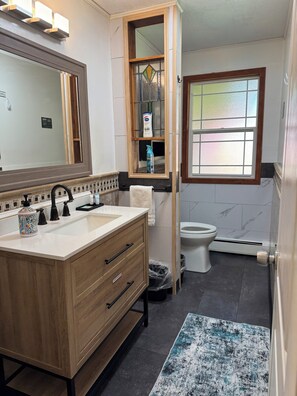 A modern bathroom with a wooden vanity, a large mirror, a toilet, and a window. - Charming 3-BR house in Juneau perfect for your getaway, minutes from the Airport (Juneau)