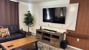 Un salon moderne avec un téléviseur à écran plat fixé au mur, une table basse en bois, un canapé en cuir marron, une grande plante en pot et un meuble de rangement en bois.