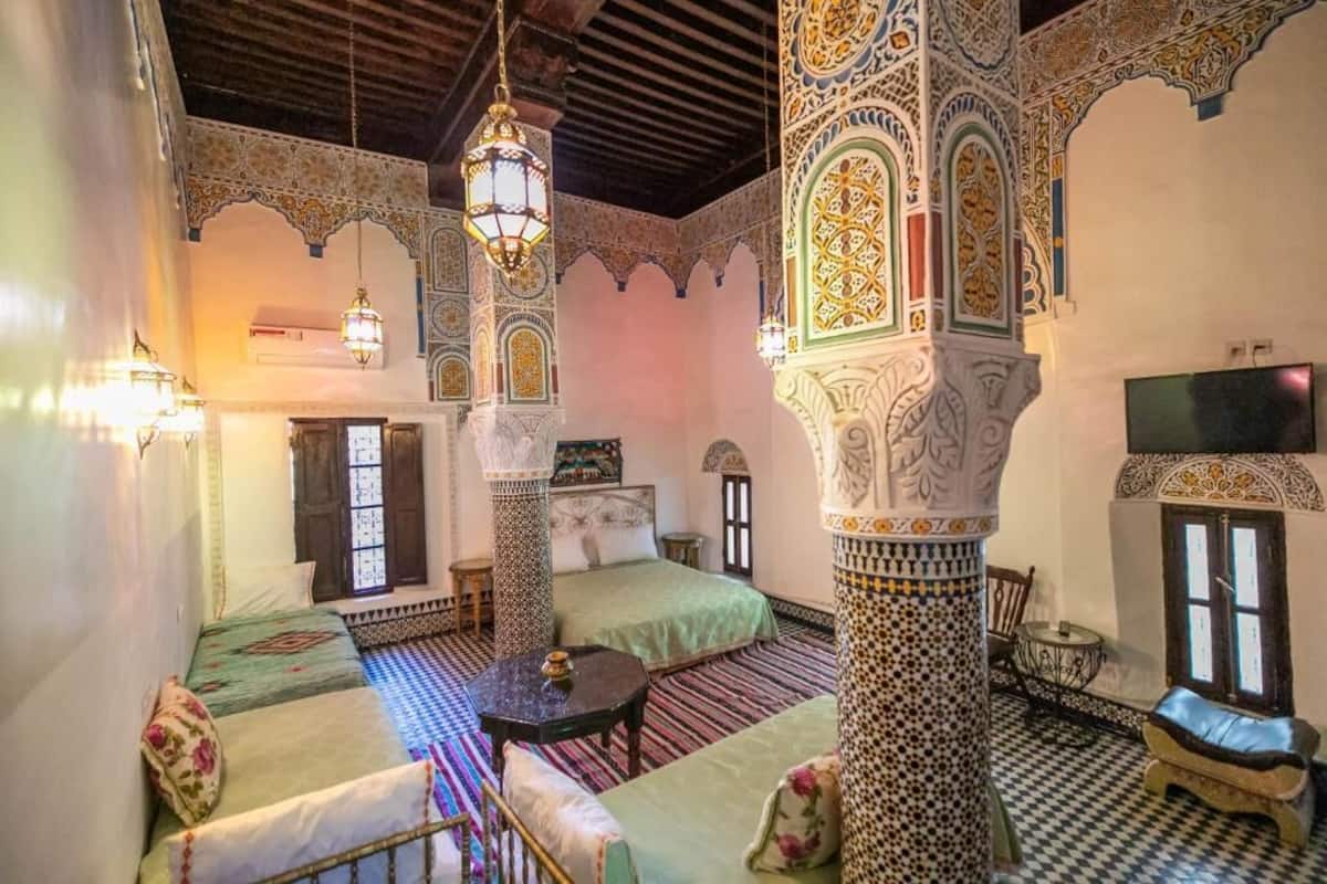A traditional Moroccan room with ornate arches, a checkered floor, and a bed with a green bedspread.