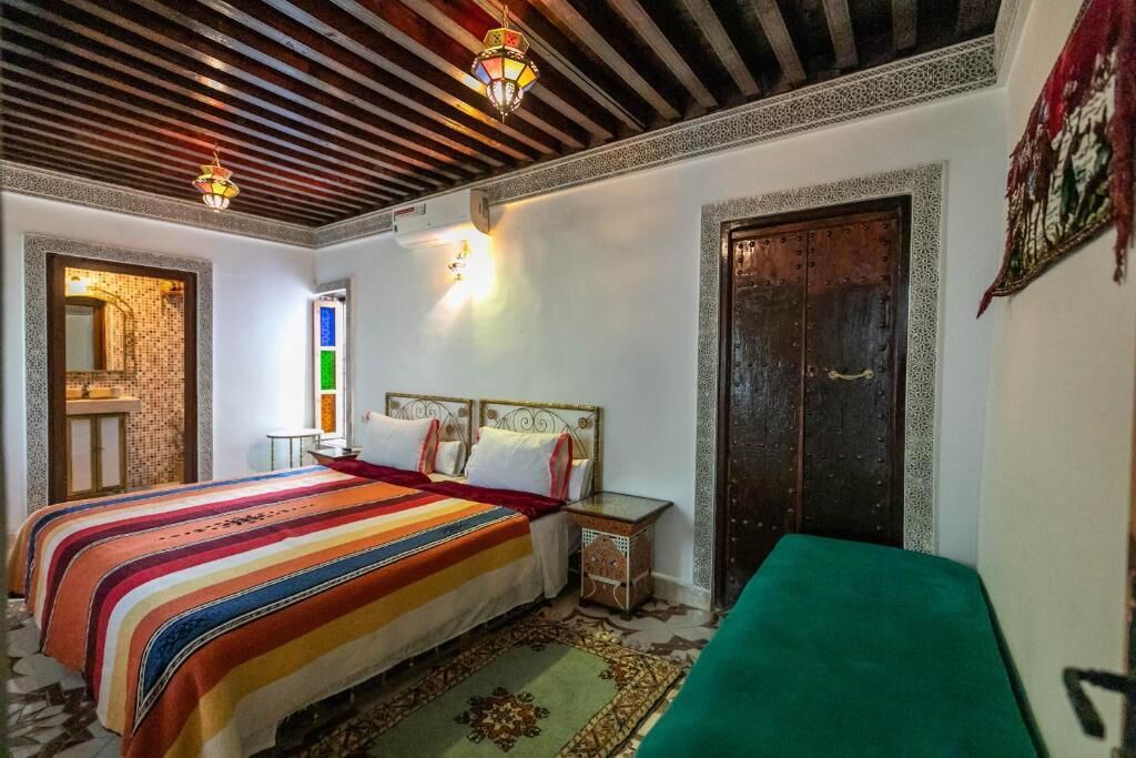 Una camera da letto con un letto grande, una poltrona verde, una porta in legno e un tappeto decorato.