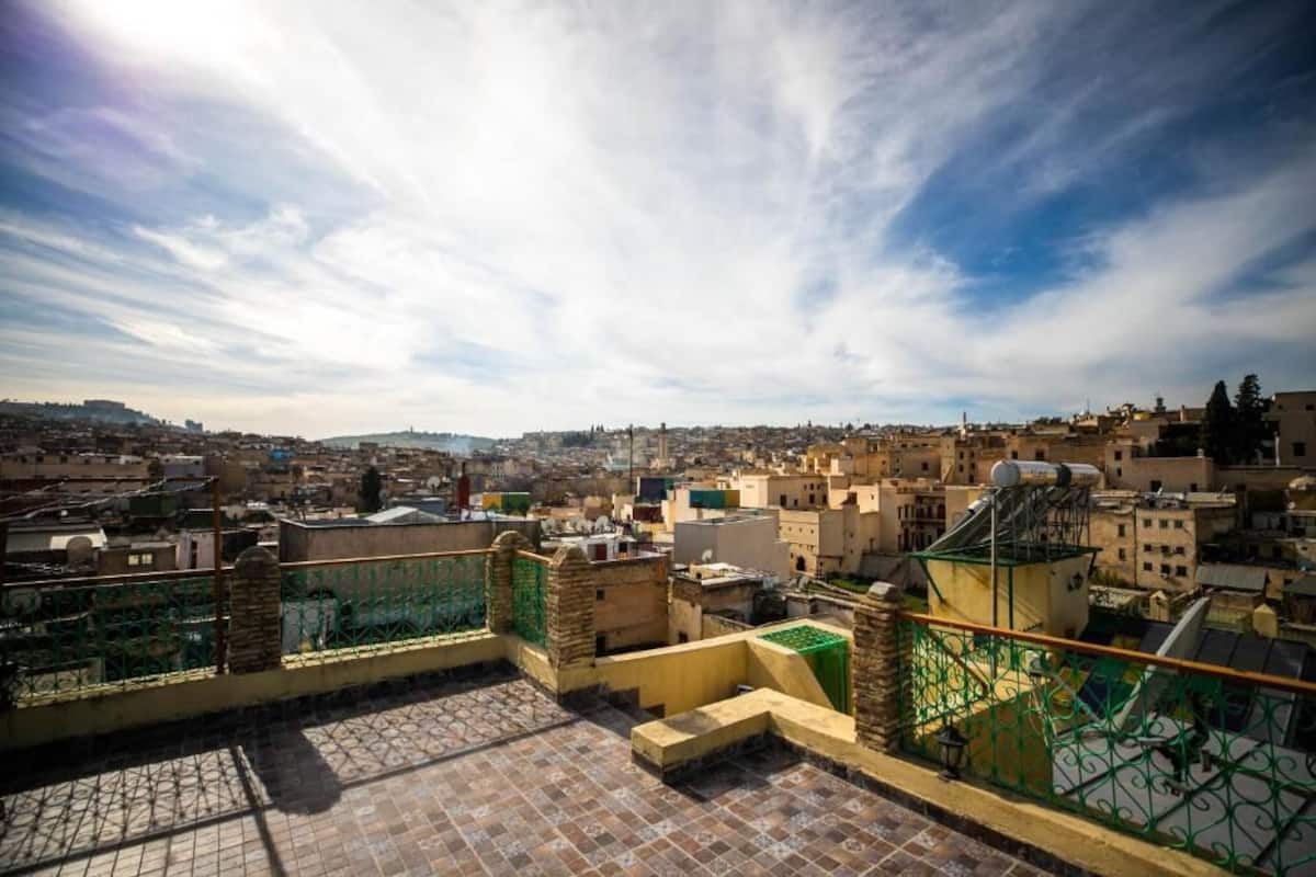 A rooftop terrace with a view of a cityscape, featuring a mix of traditional and modern buildings, and a clear sky.