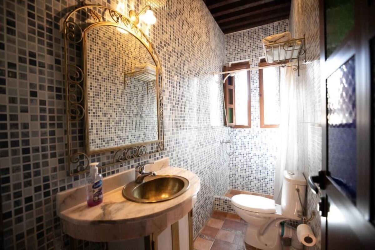 A bathroom with mosaic tile walls, a sink with a mirror, and a toilet.