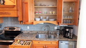 Una cocina con armarios de madera, encimeras de granito, un lavamanos de acero inoxidable, una cafetera y un lavavajillas.