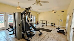 A gym with various exercise equipment, ceiling fans, and a view of the outside through glass doors.