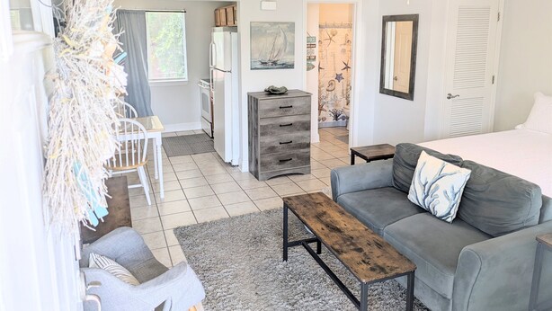 A well-lit living room with a grey sofa, a wooden coffee table, and a dining area with a table and chairs.