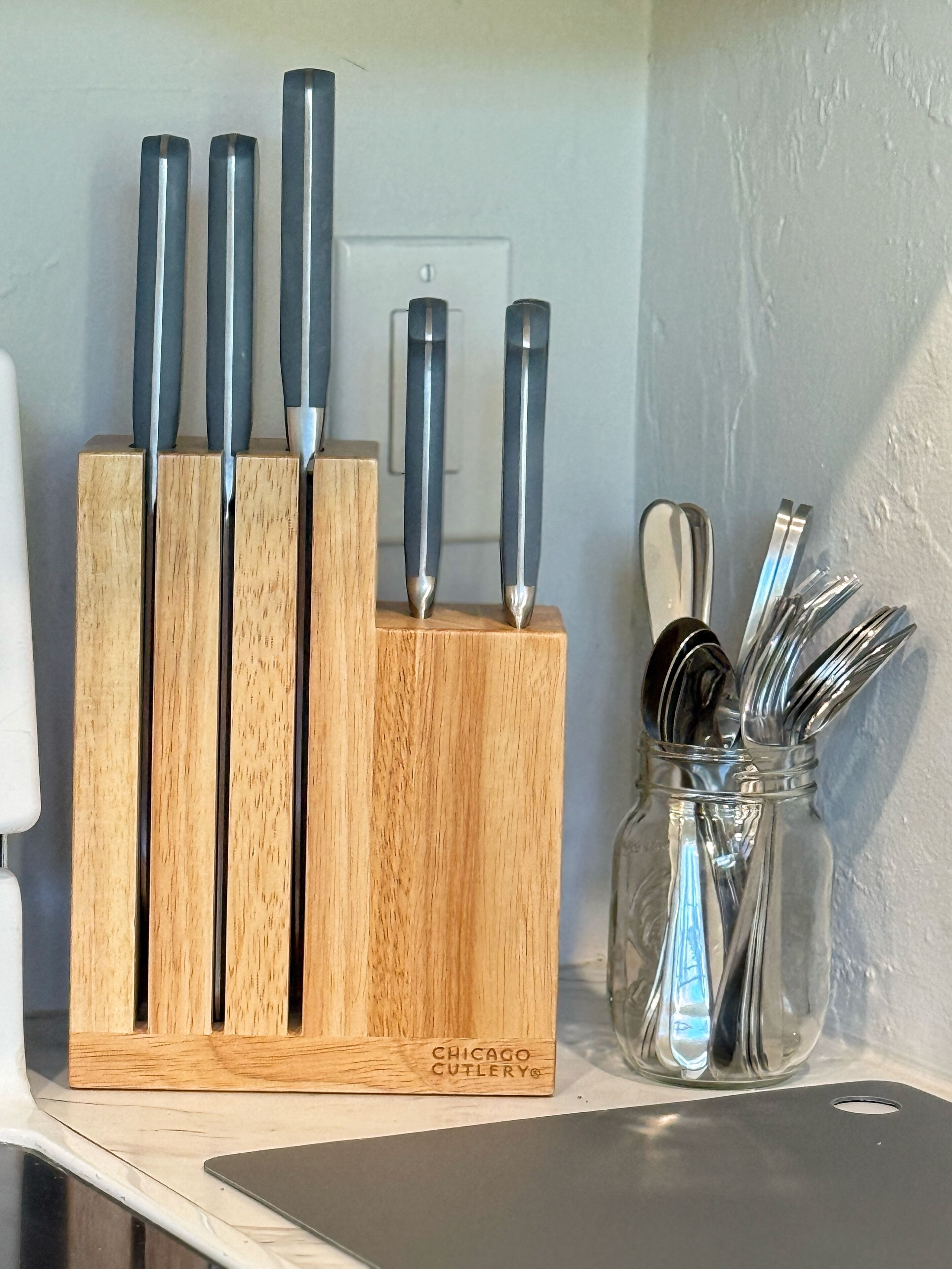 A wooden knife block with several knives and a glass jar with utensils.