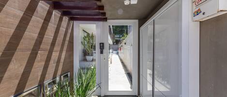 A narrow hallway with a door leading to a balcony, a potted plant, and a mailbox on the right.