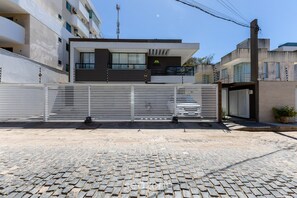 A modern building with a gated entrance, a paved driveway, and a cobblestone street. - House w/ Terrace & BBQ 100m From the sea Ellc0000 (Ilhéus)