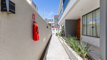A narrow corridor with a fire hydrant, a red emergency exit sign, and a planter with green plants.