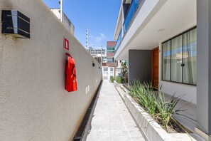 A narrow corridor with a fire hydrant, a red emergency exit sign, and a planter with green plants. - House w/ Terrace & BBQ 100m From the sea Ellc0000 (Ilhéus)