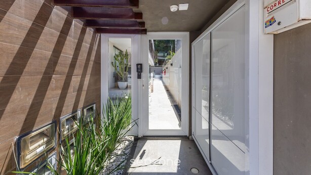 A narrow hallway with a door leading to a bright outdoor area, a mailbox, and a potted plant.