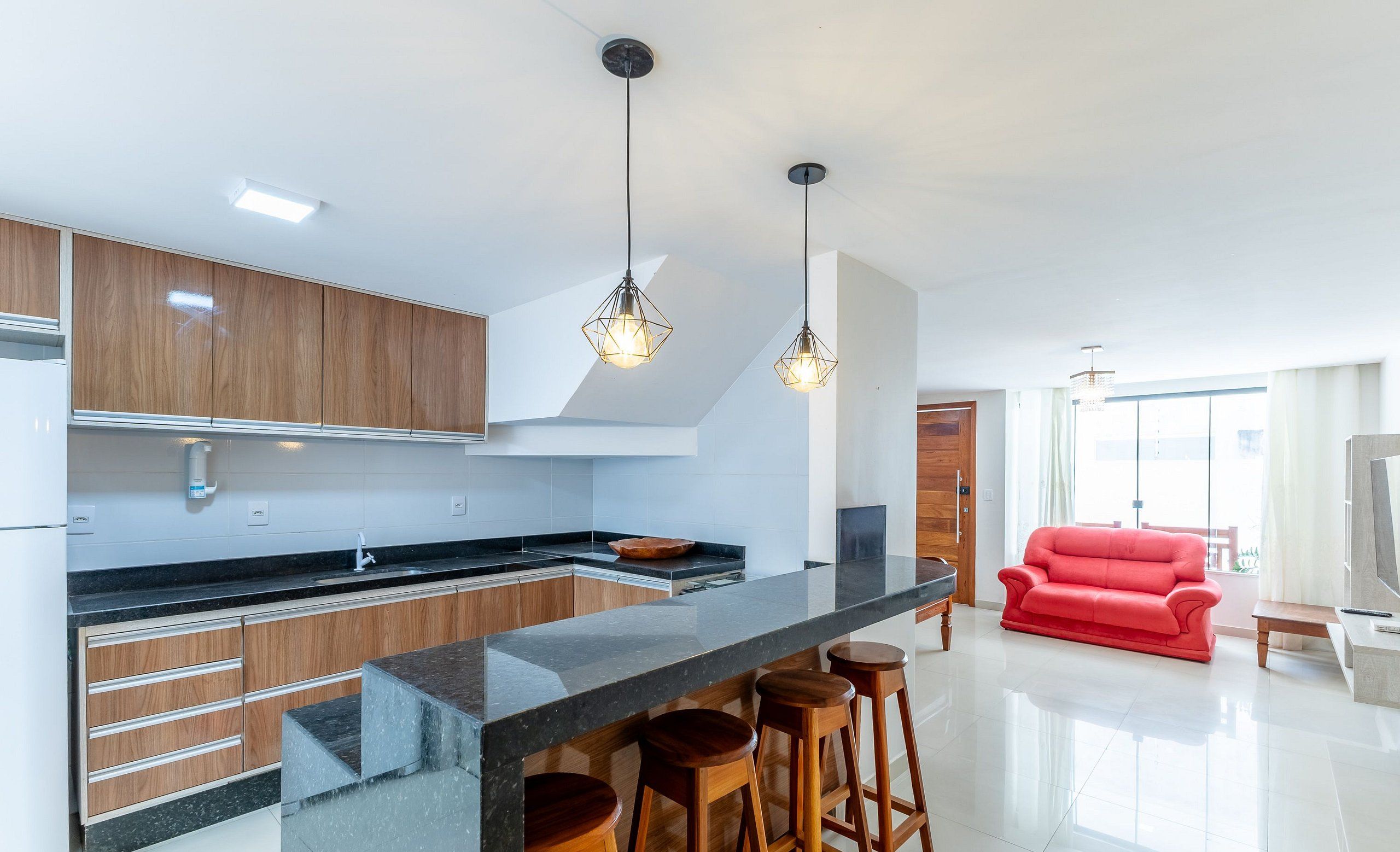 Uma cozinha moderna com armários de madeira, bancada preta e sofá vermelho na sala de estar.